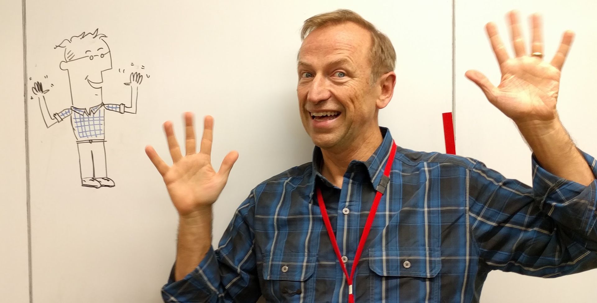 Jerry Michalski in a plaid shirt is standing in front of a whiteboard with a drawing of a man on it.