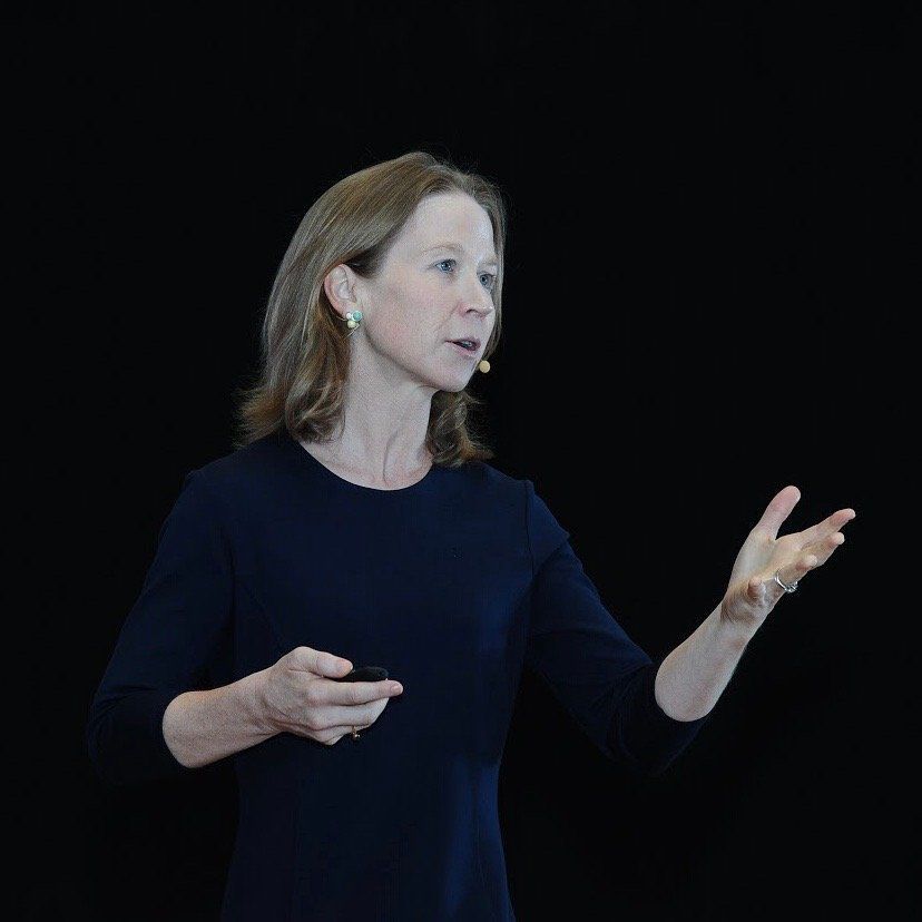 April Rinne in a blue dress is standing in front of a black background.