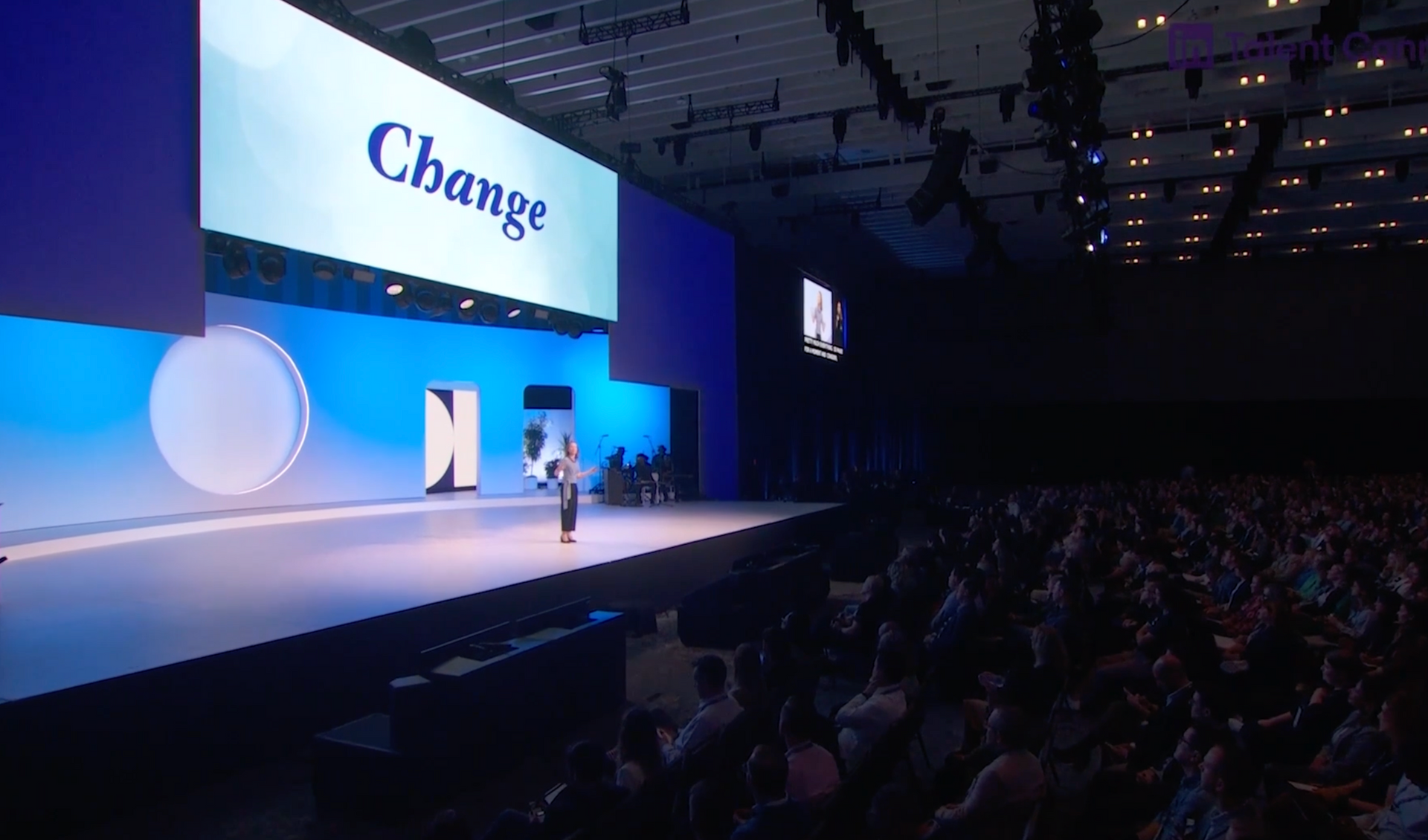 April Rinne standing on a stage in front of a large screen with the word change on it