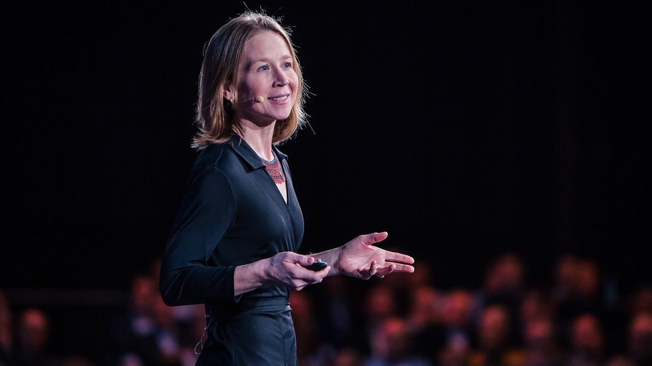April Rinne is giving a speech on a stage in front of a crowd.