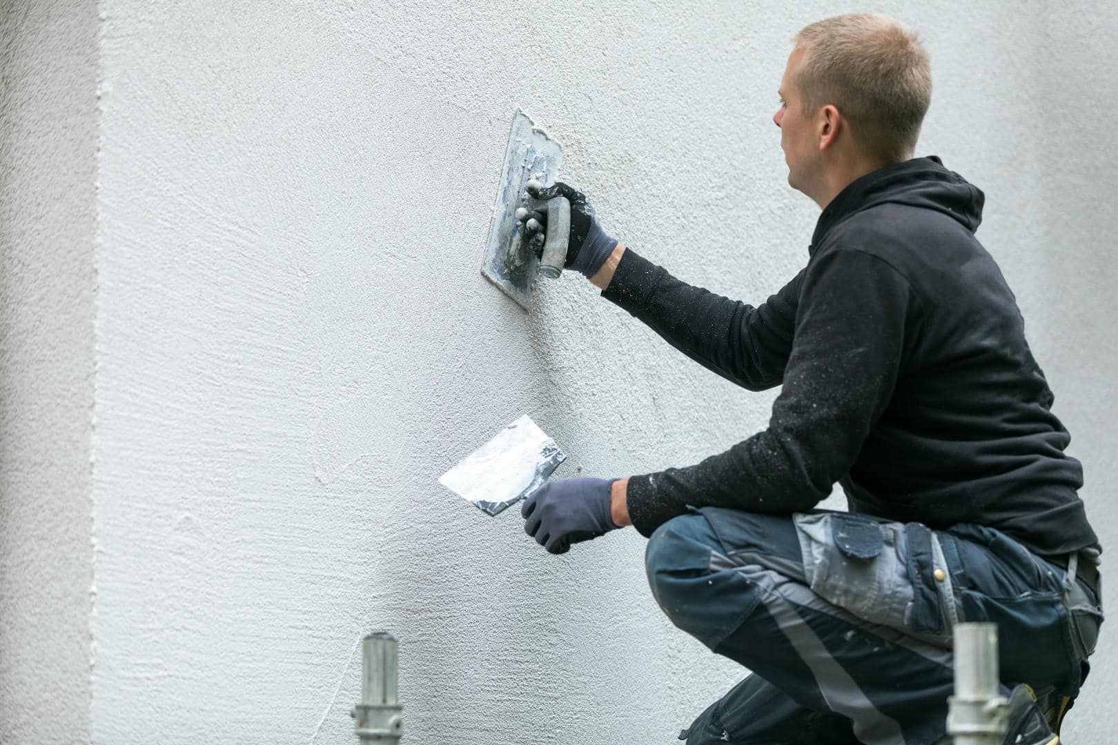 A man is kneeling down and plastering a wall with a spatula.