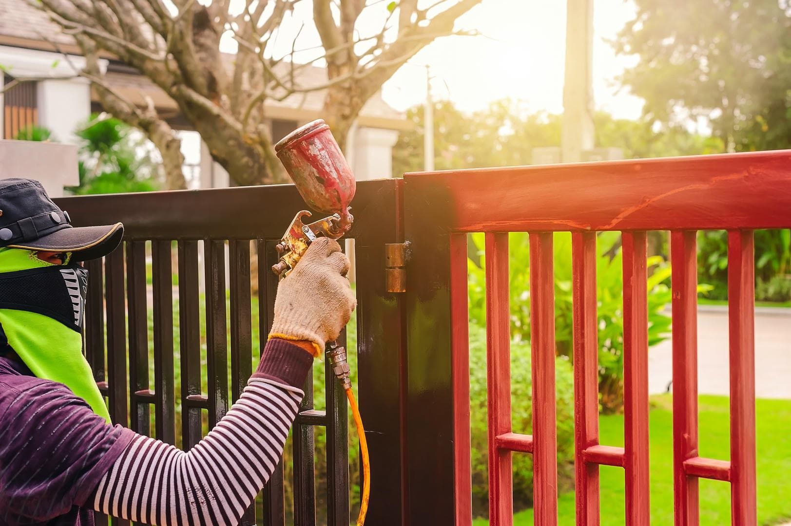 A man is spraying paint on a metal fence.