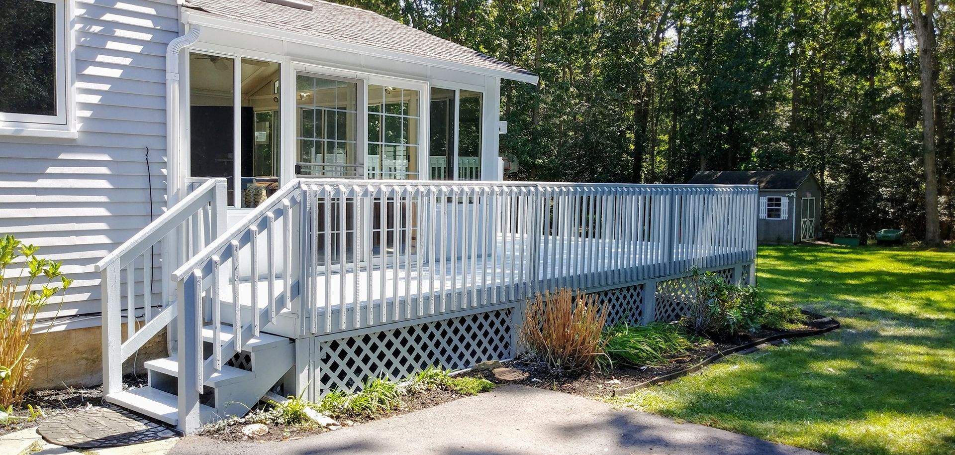 A light gray house with a deck and screened porch surrounded by trees and grass.
