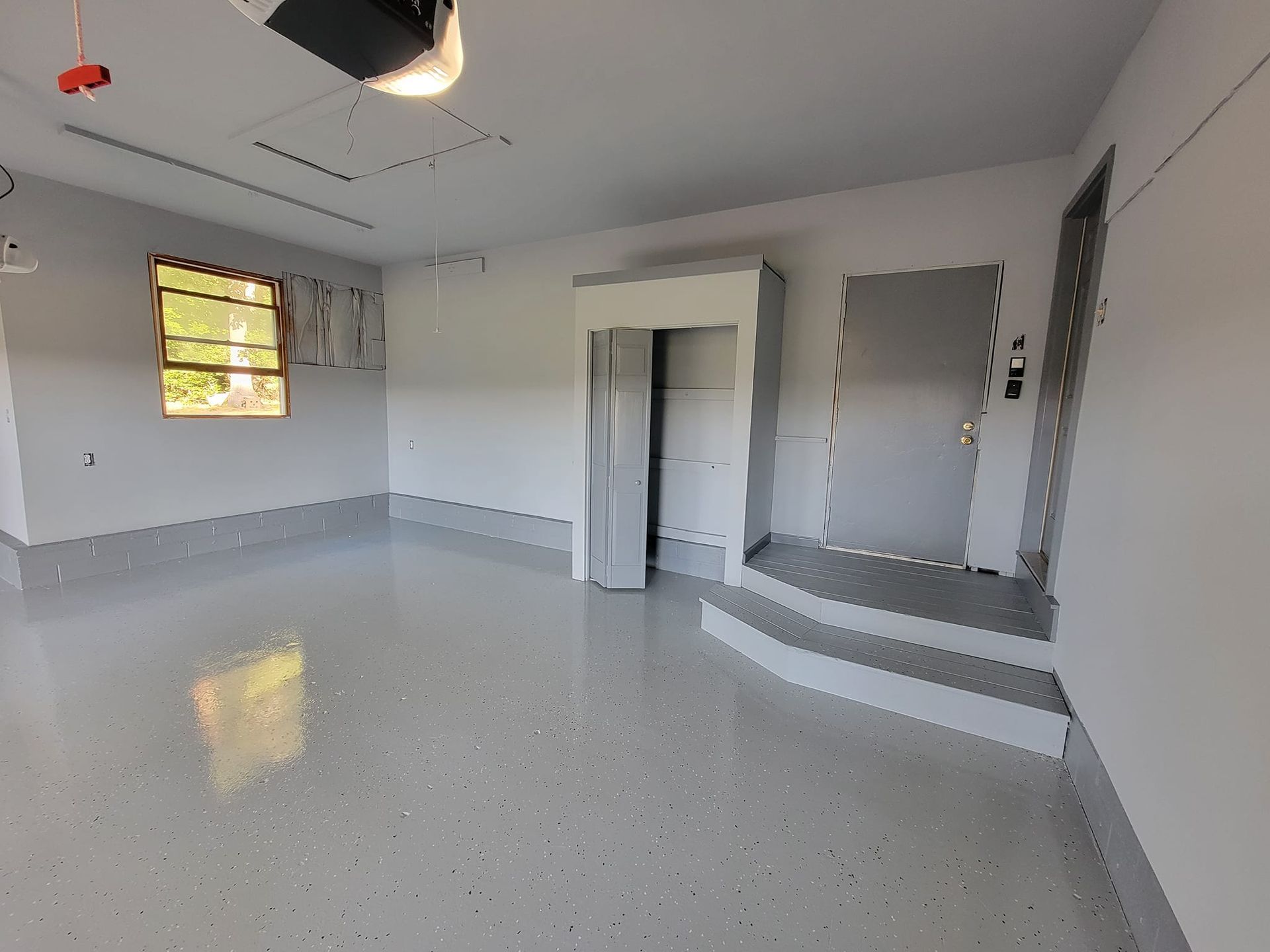 Empty garage with gray epoxy floor, white walls, a window, and a gray door.