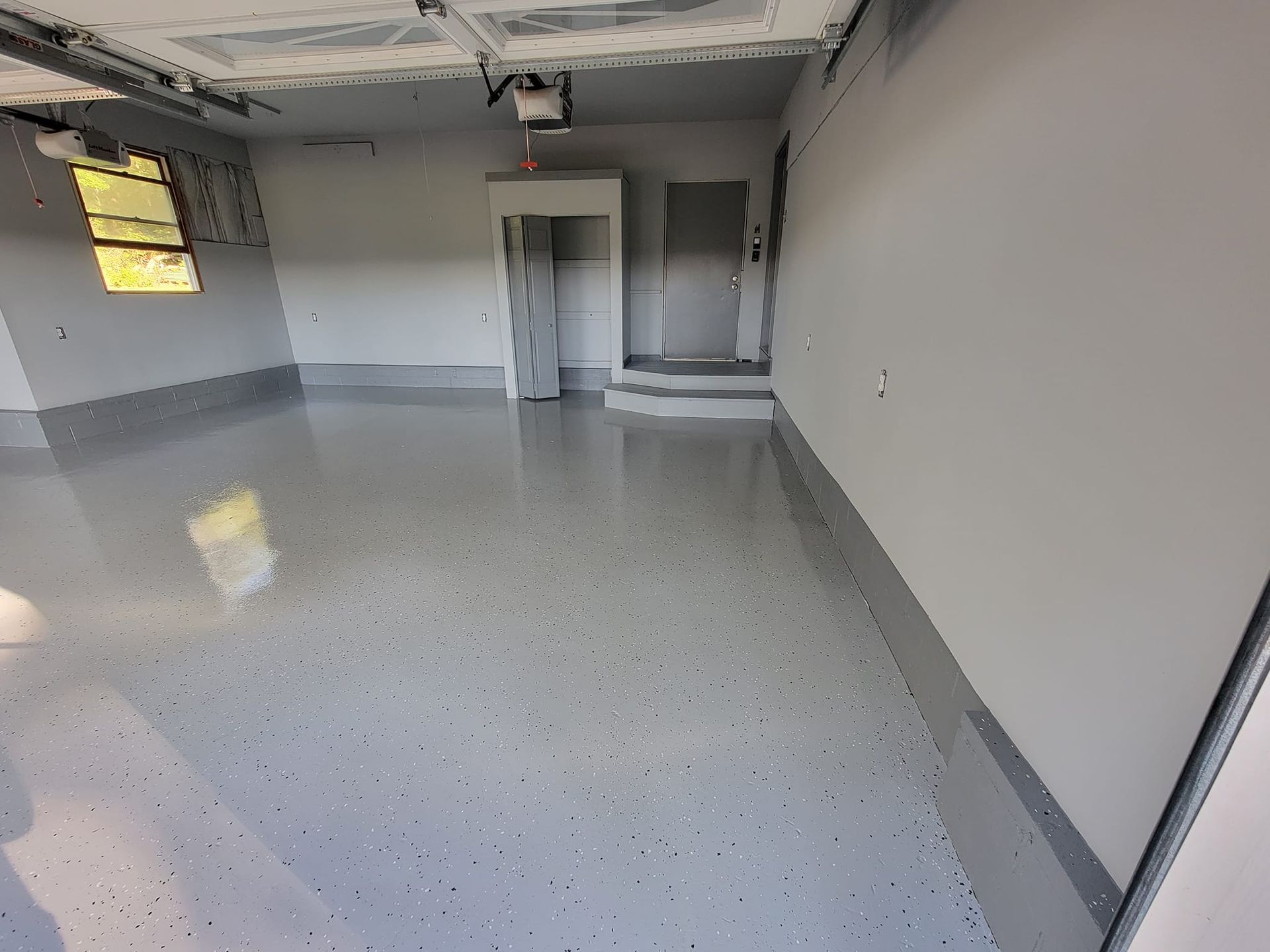 A newly painted garage with a speckled gray epoxy floor and light gray walls.