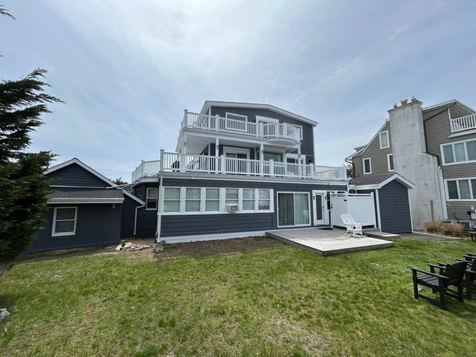 Coastal home with multiple levels, gray exterior, white trim, and balconies overlooking the lawn.