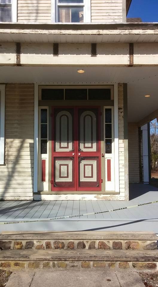 Exterior view of an old house with a red door and a porch.