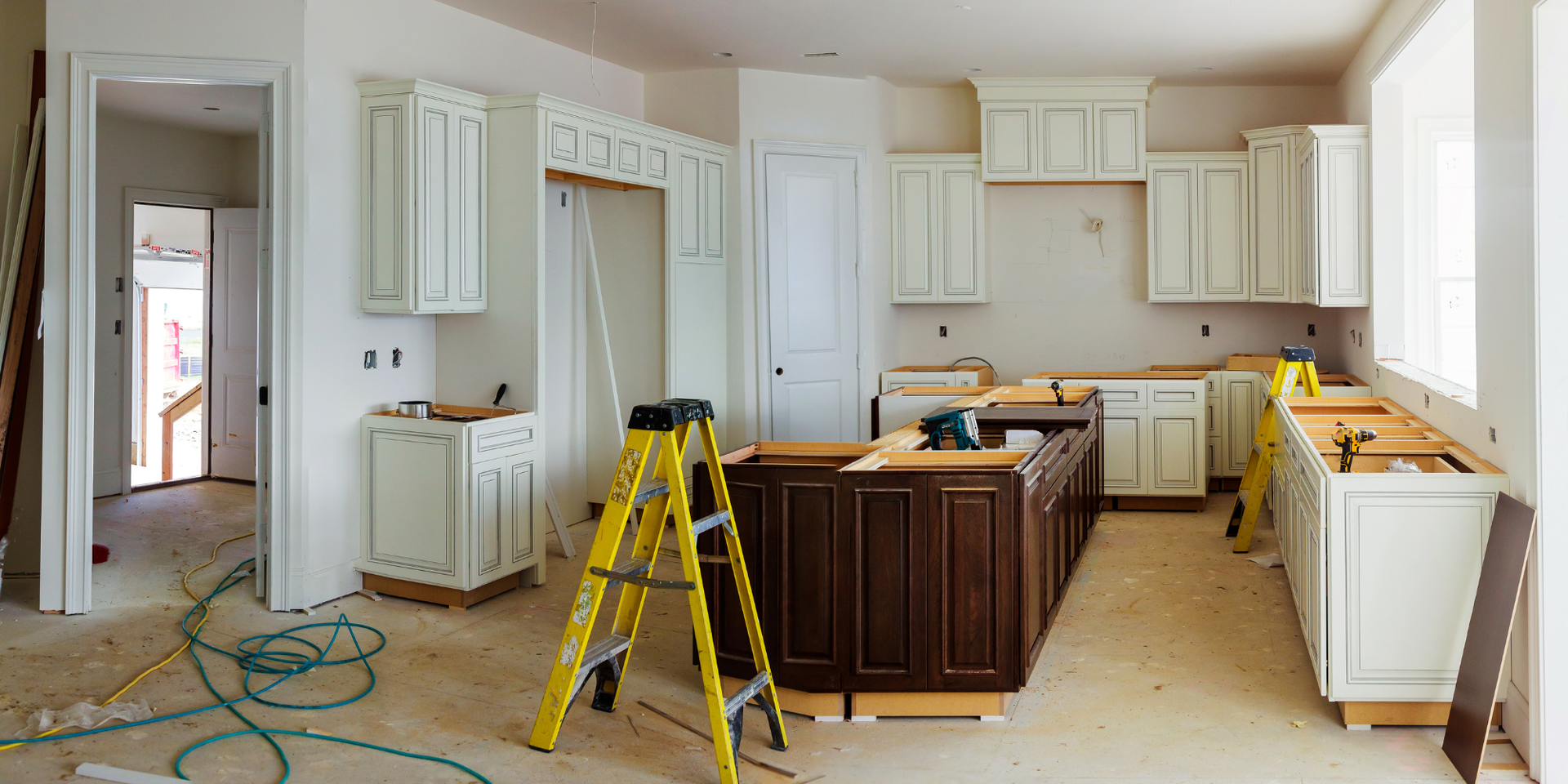 Kitchen under construction, with white and dark brown cabinets, a yellow ladder, and tools.