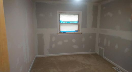 Room with walls undergoing drywall repair; window, beige carpet.