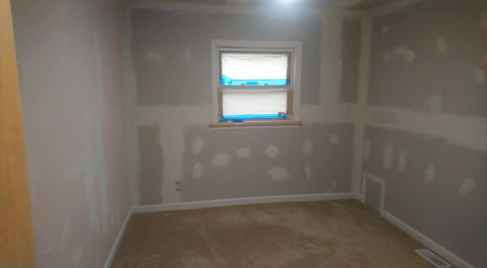 Room with walls undergoing drywall repair; window, beige carpet.