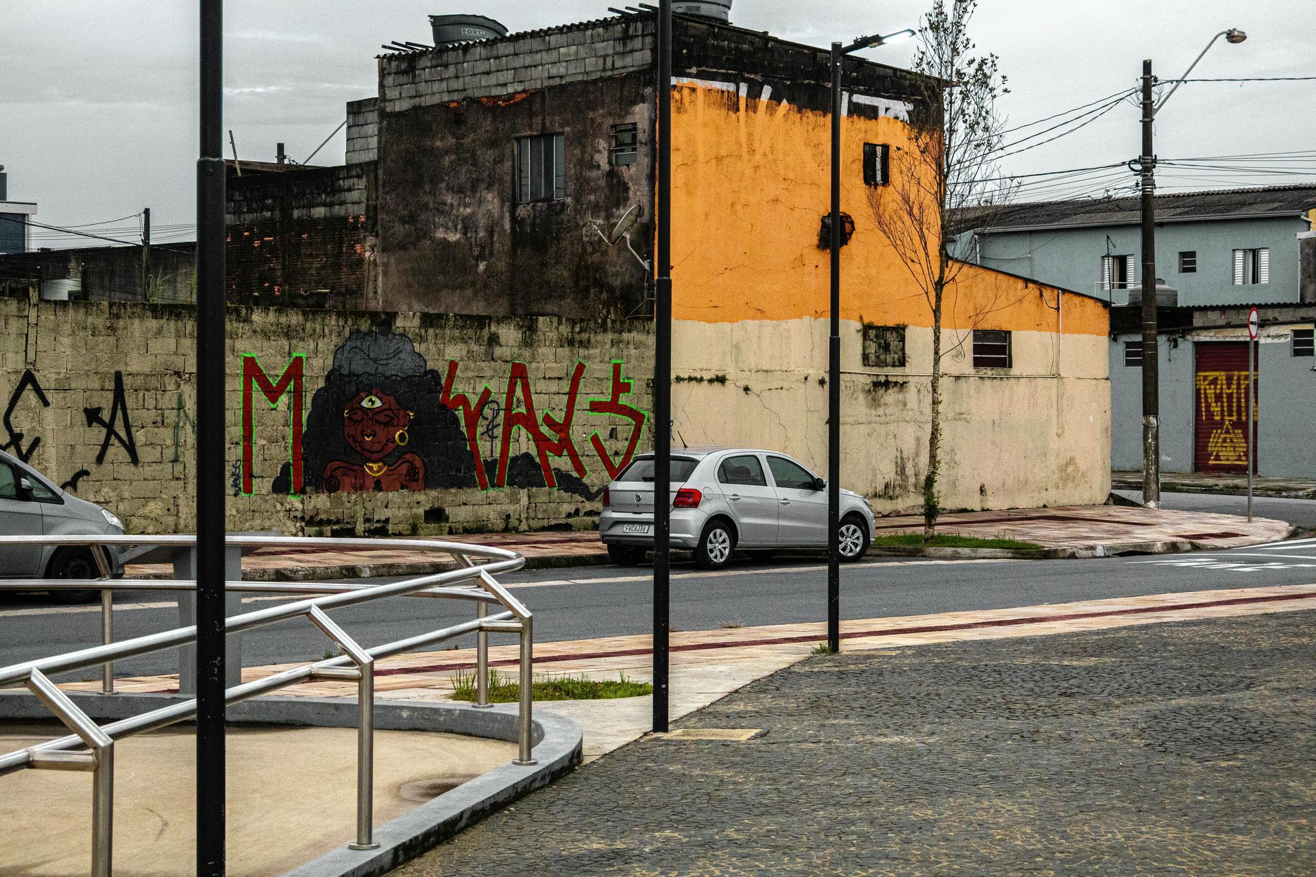 Street scene with graffiti on building, a car parked on the street, and a pedestrian walkway.