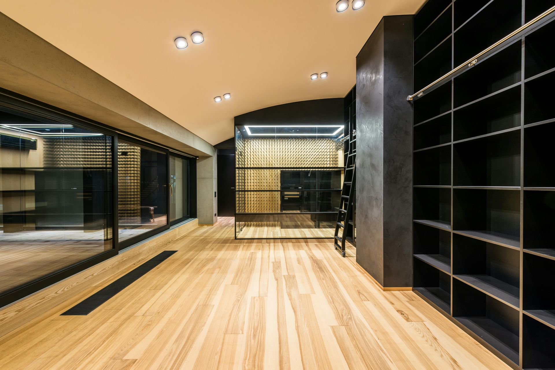 Wooden-floored, modern room with large windows, black shelving units, and built-in lighting.