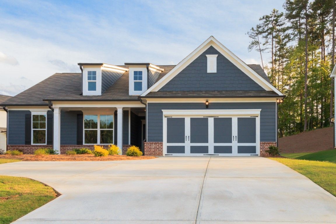 Blue house with a driveway, garage, and dormers under a sunny sky.