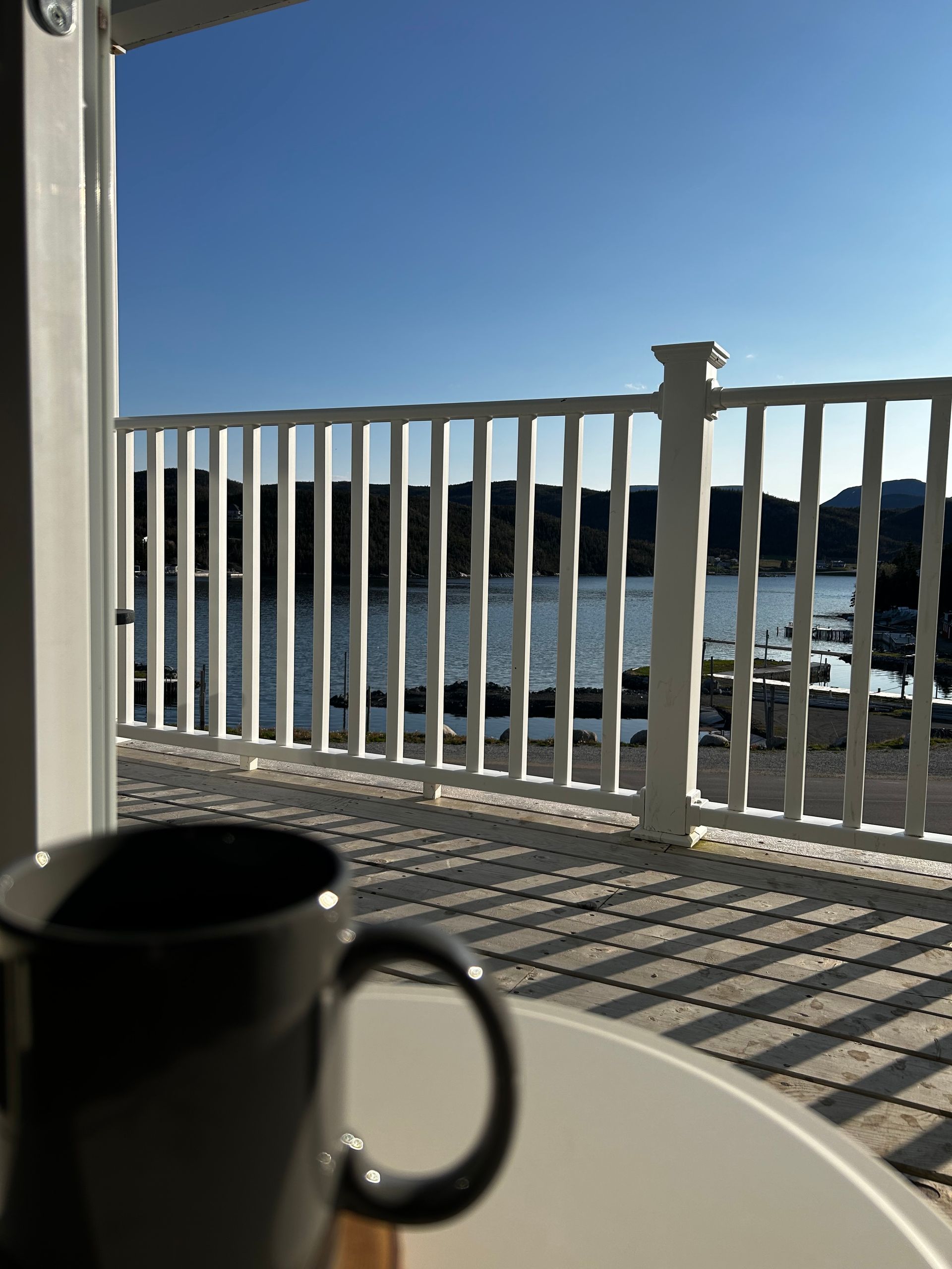 A coffee mug sits on a table in front of a balcony overlooking a body of water