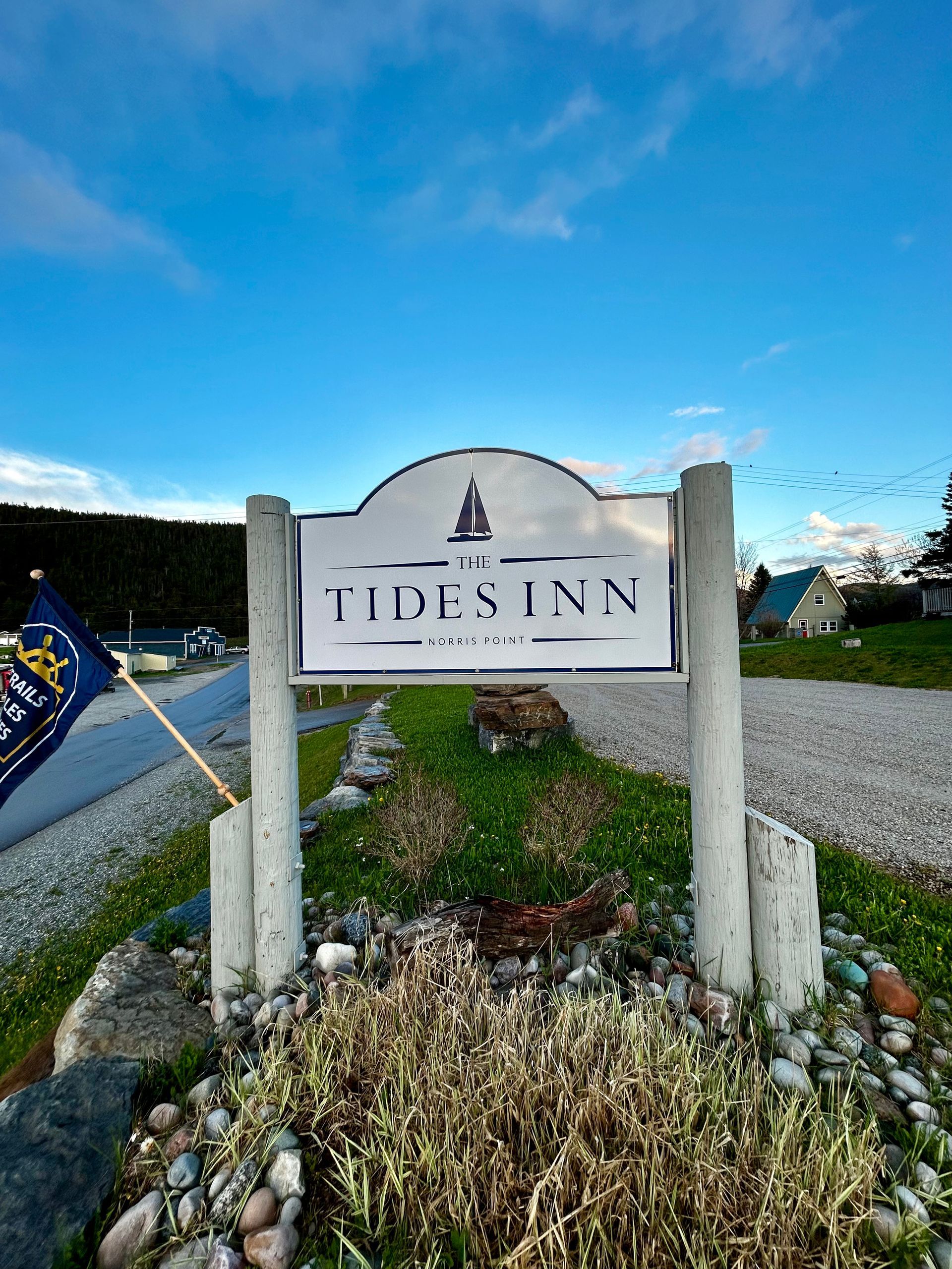 A sign for the tide inn is sitting on top of a gravel road.