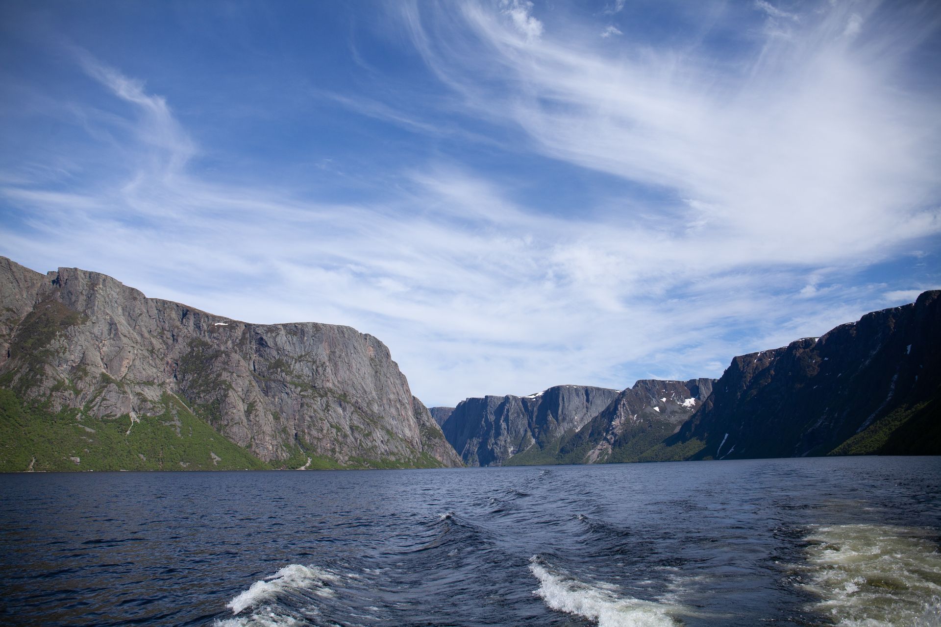 A boat is going through a lake with mountains in the background