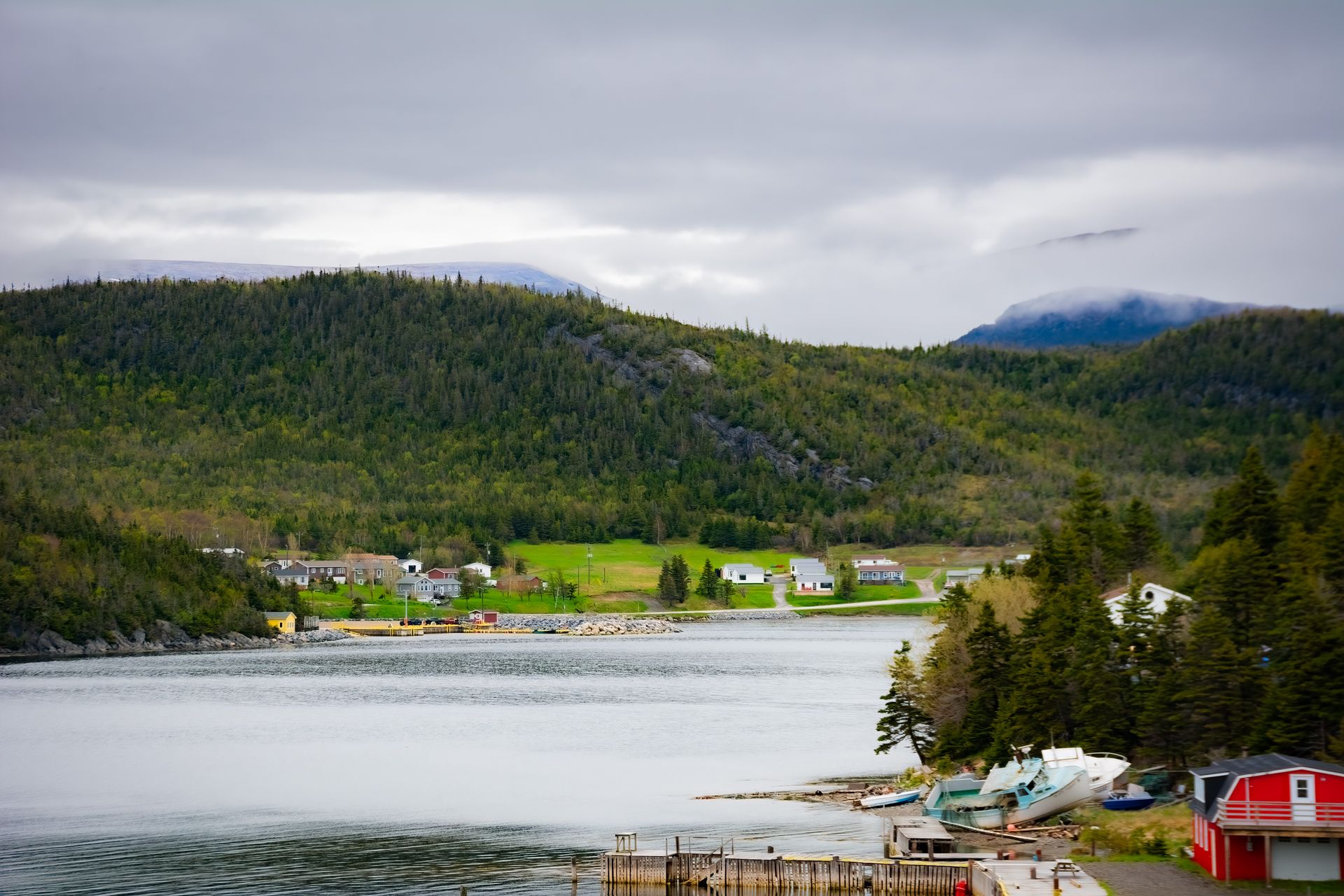 A red barn sits on the shore of a lake with mountains in the background.