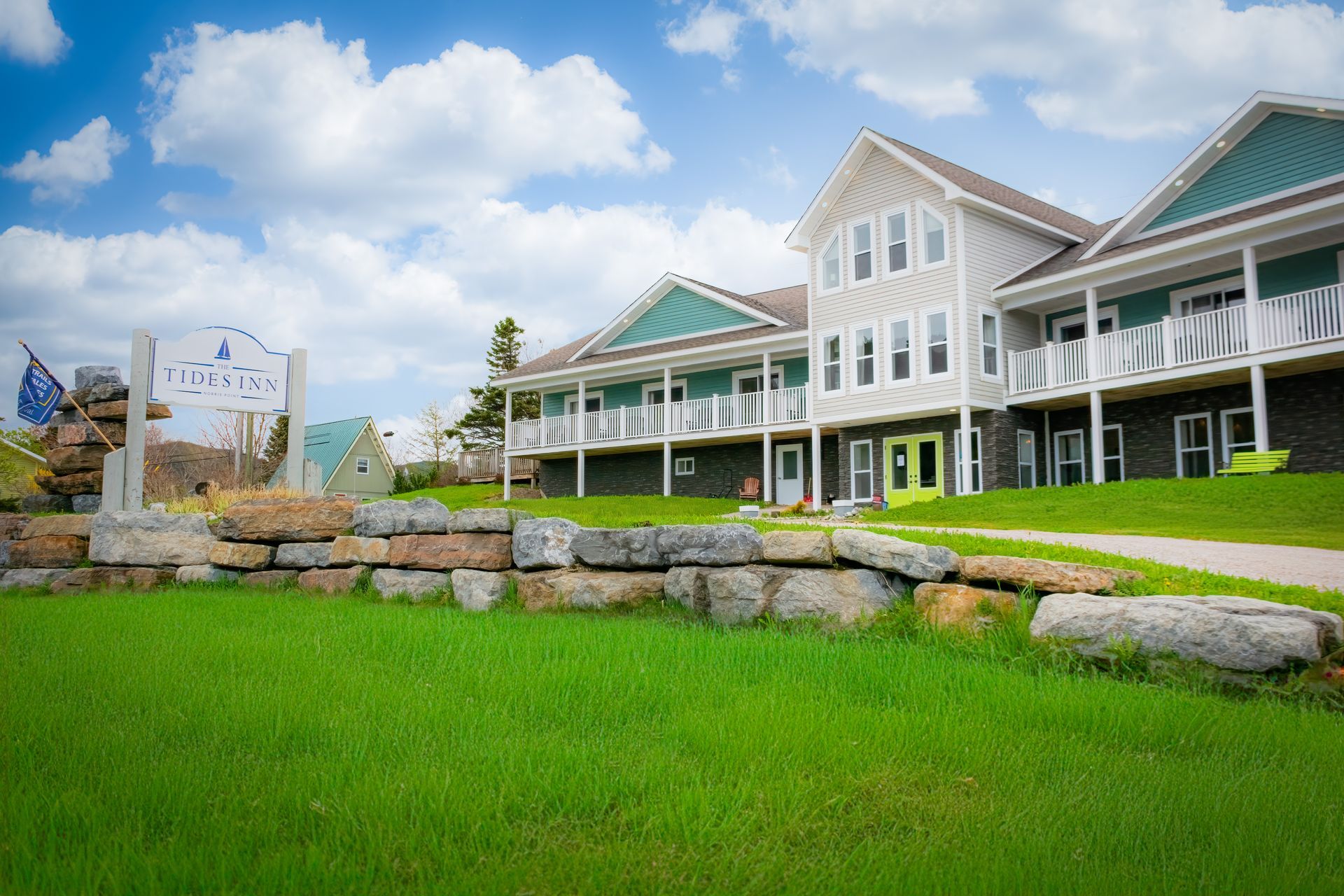 A large white and green house is sitting on top of a lush green hill.