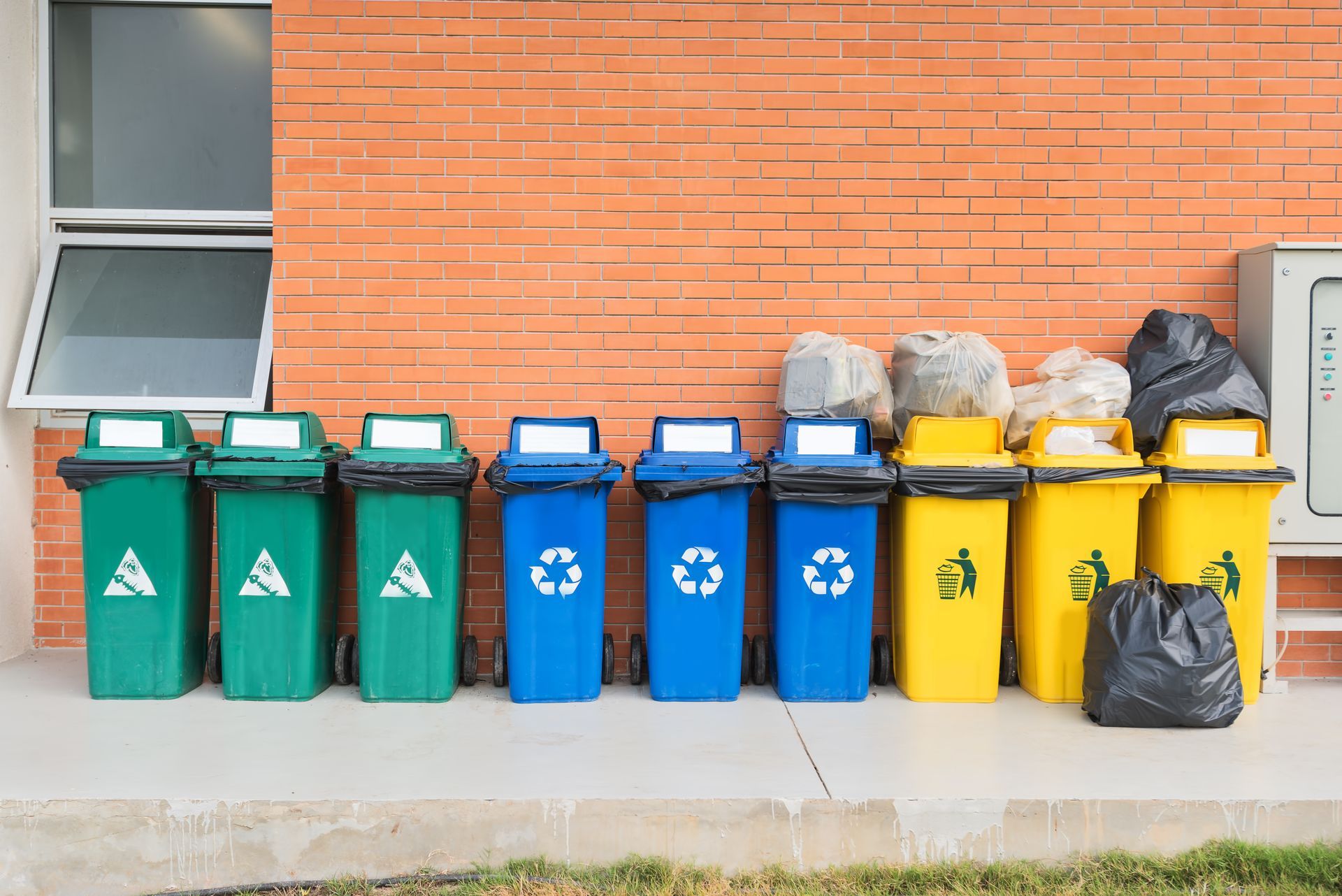 A row of trash cans are lined up in front of a brick building.