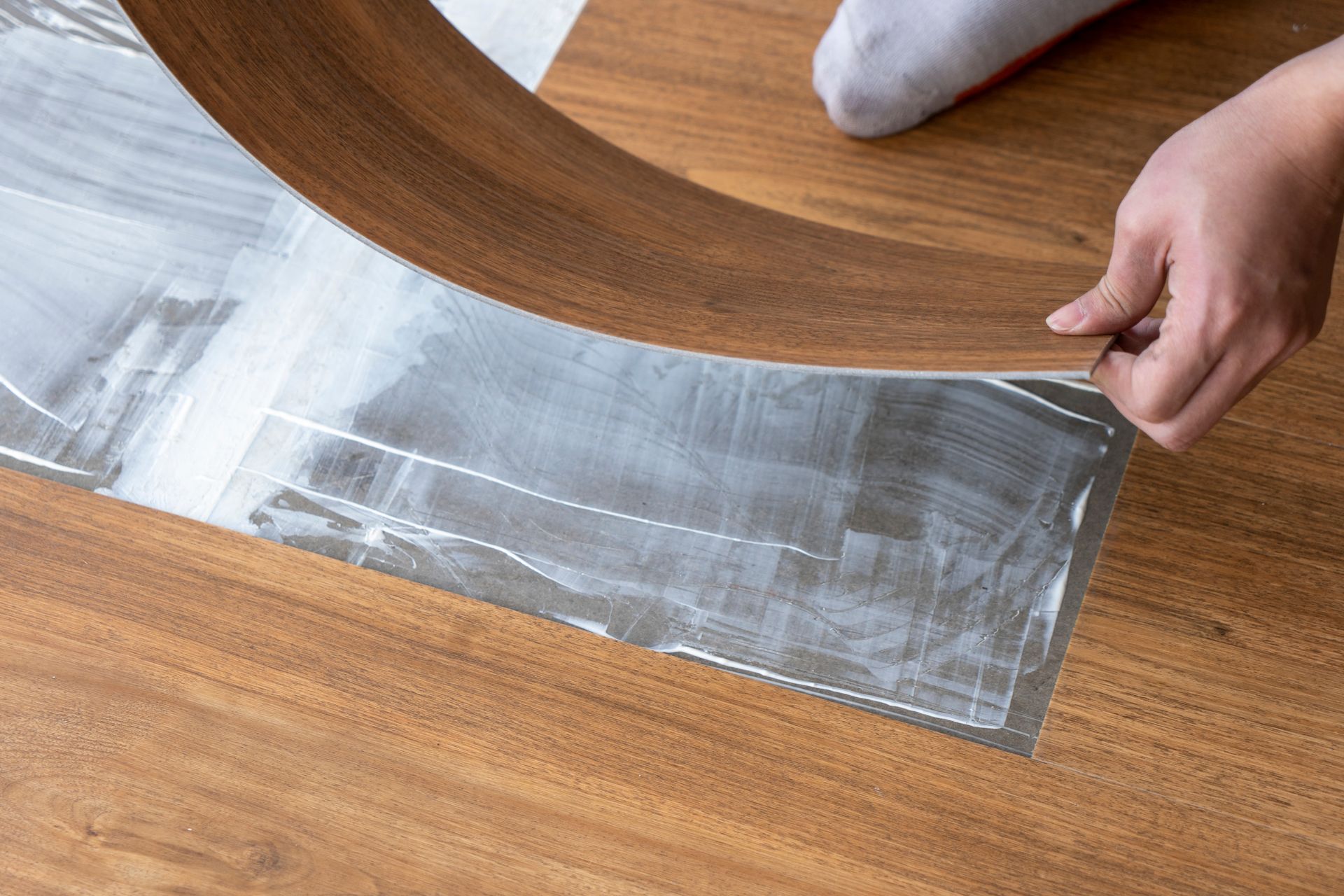 A person is laying a piece of vinyl flooring on a wooden floor.