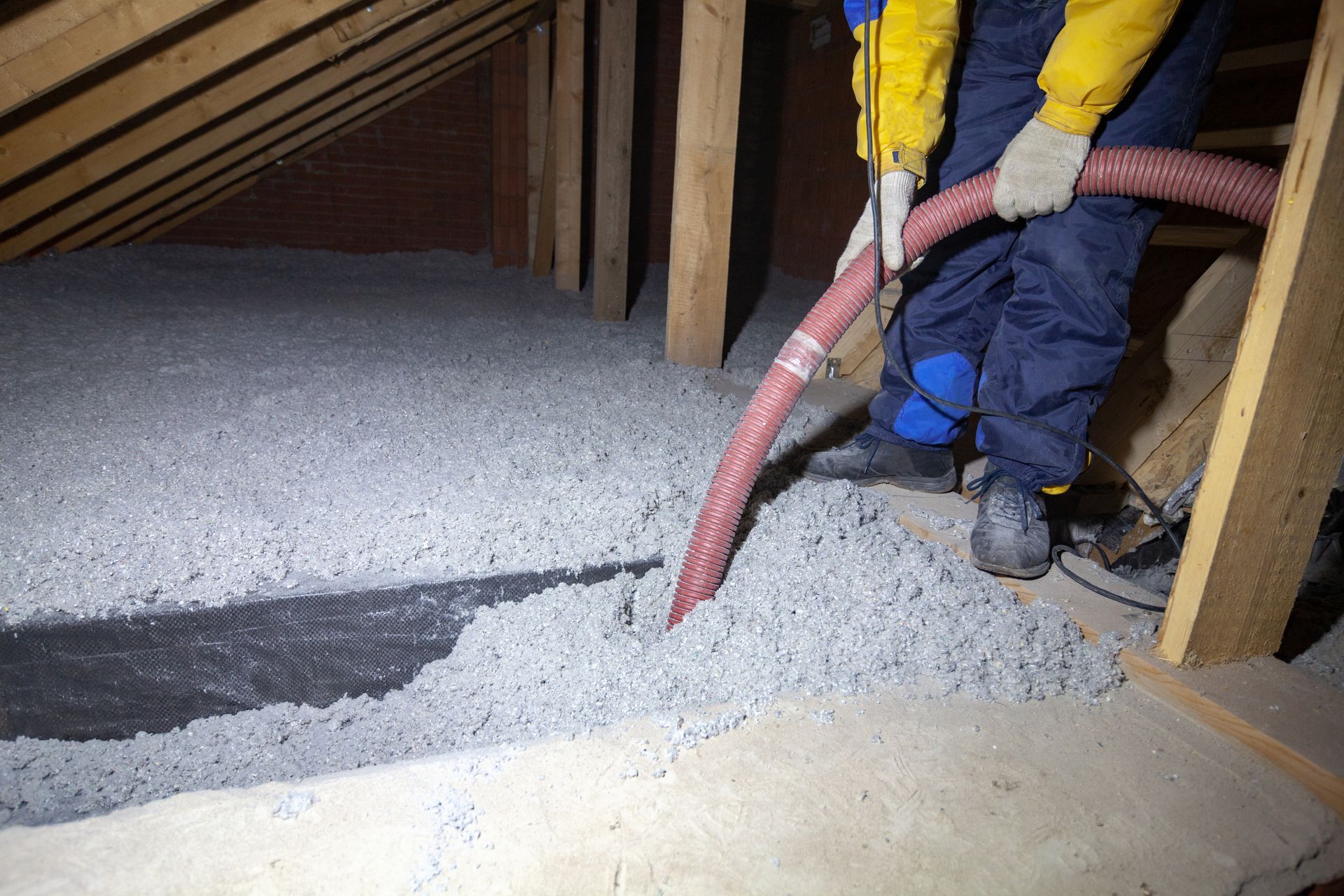 A man is blowing insulation into an attic with a vacuum hose.