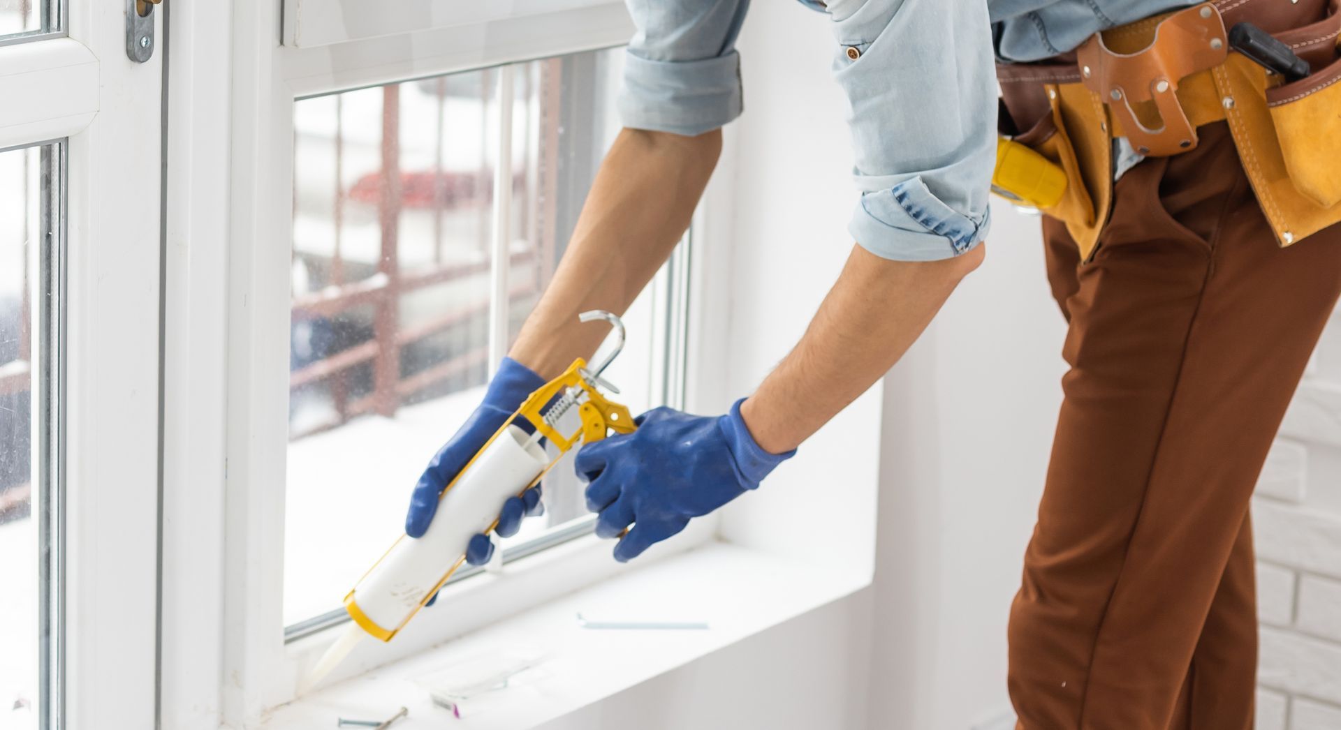A man is applying sealant to a window.