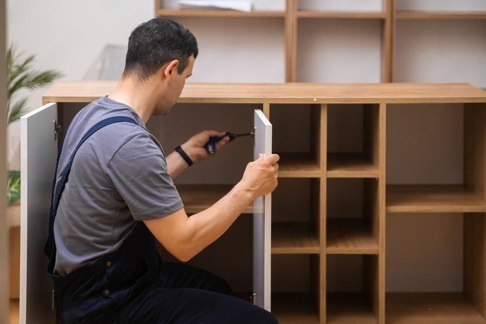 A man is fixing a cabinet with a screwdriver.