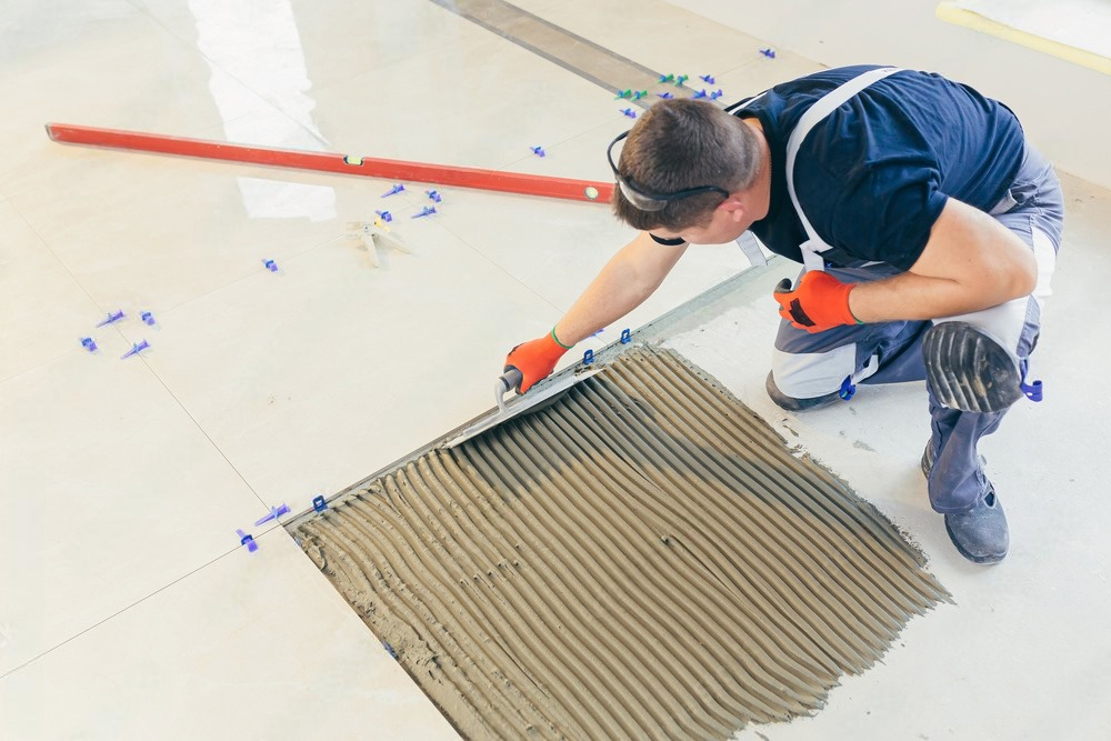 A man is applying tile adhesive to a tile floor.