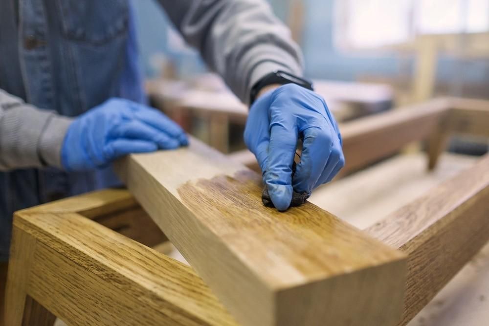 A person wearing blue gloves is painting a piece of wood.