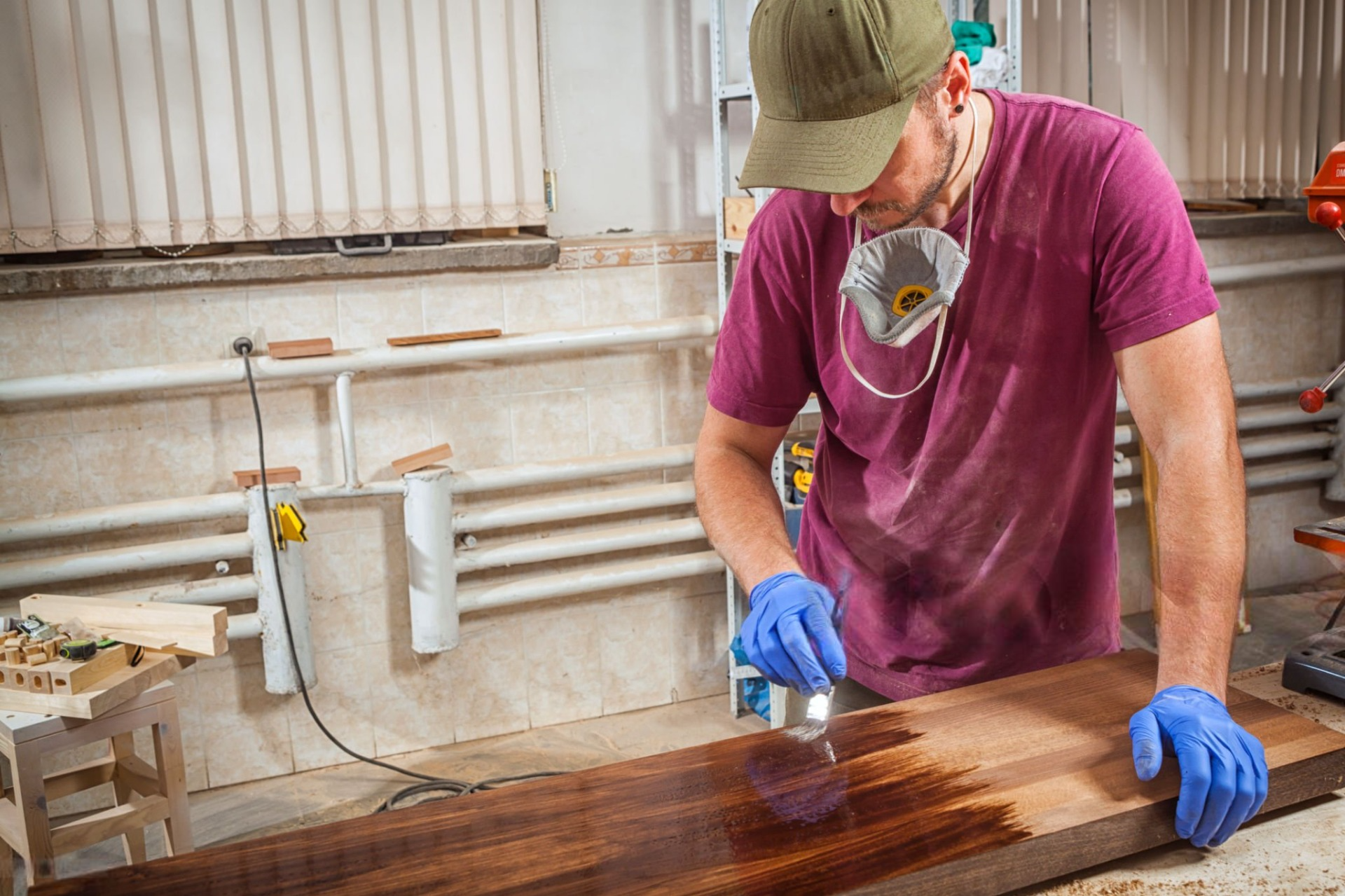 A man is painting a piece of wood in a workshop.