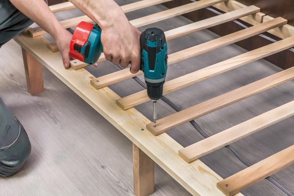 A man is using a drill and a tape measure to build a bed frame.