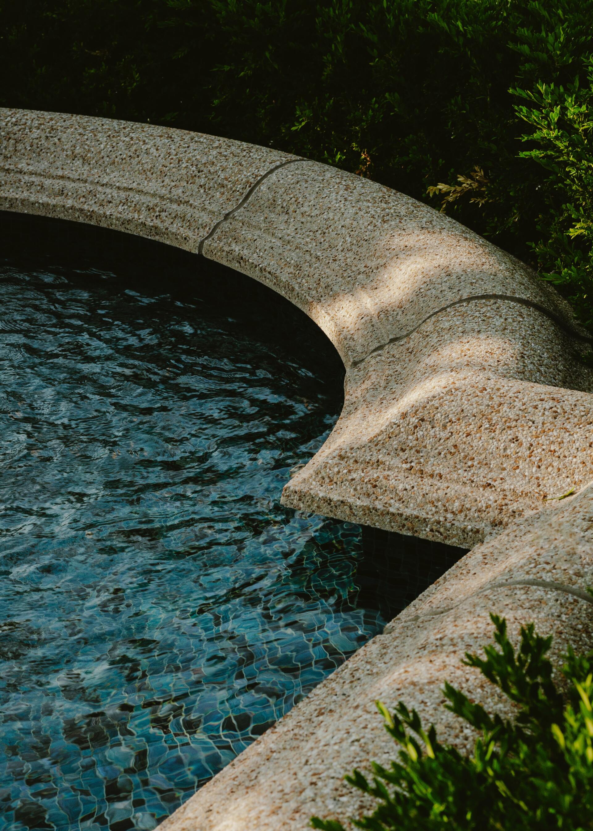 A close up of a swimming pool with a concrete border surrounded by trees.