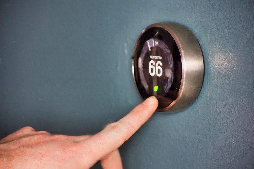 A person is pressing a button on a thermostat on a wall.