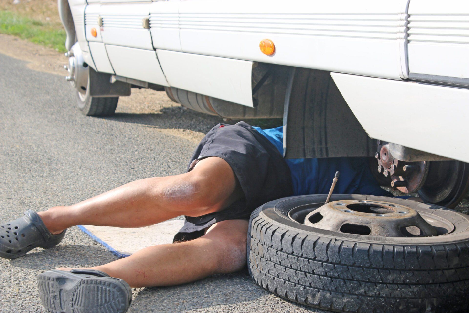 A man is laying under a vehicle with a tire on the ground