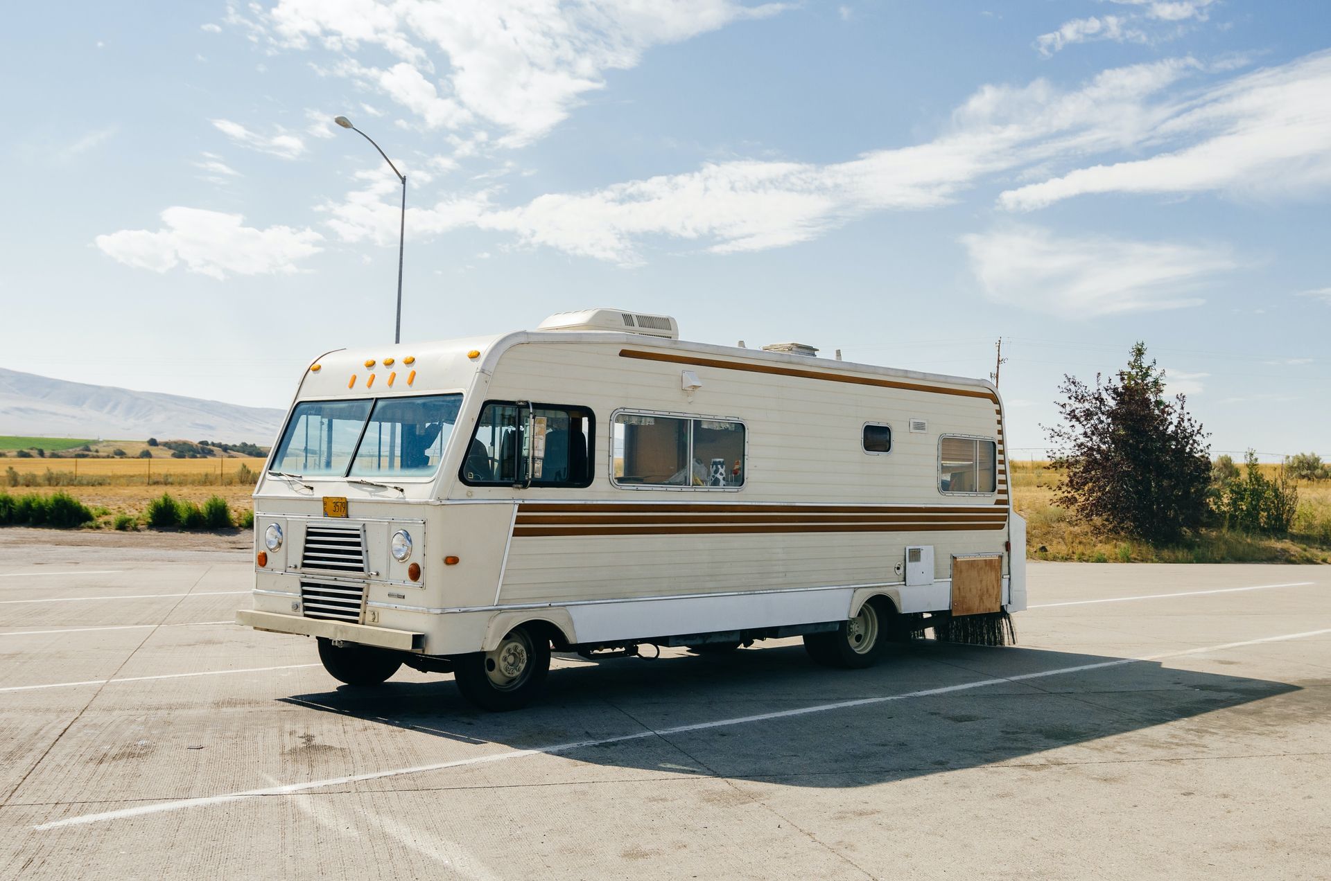 A white and brown rv is parked in a parking lot.