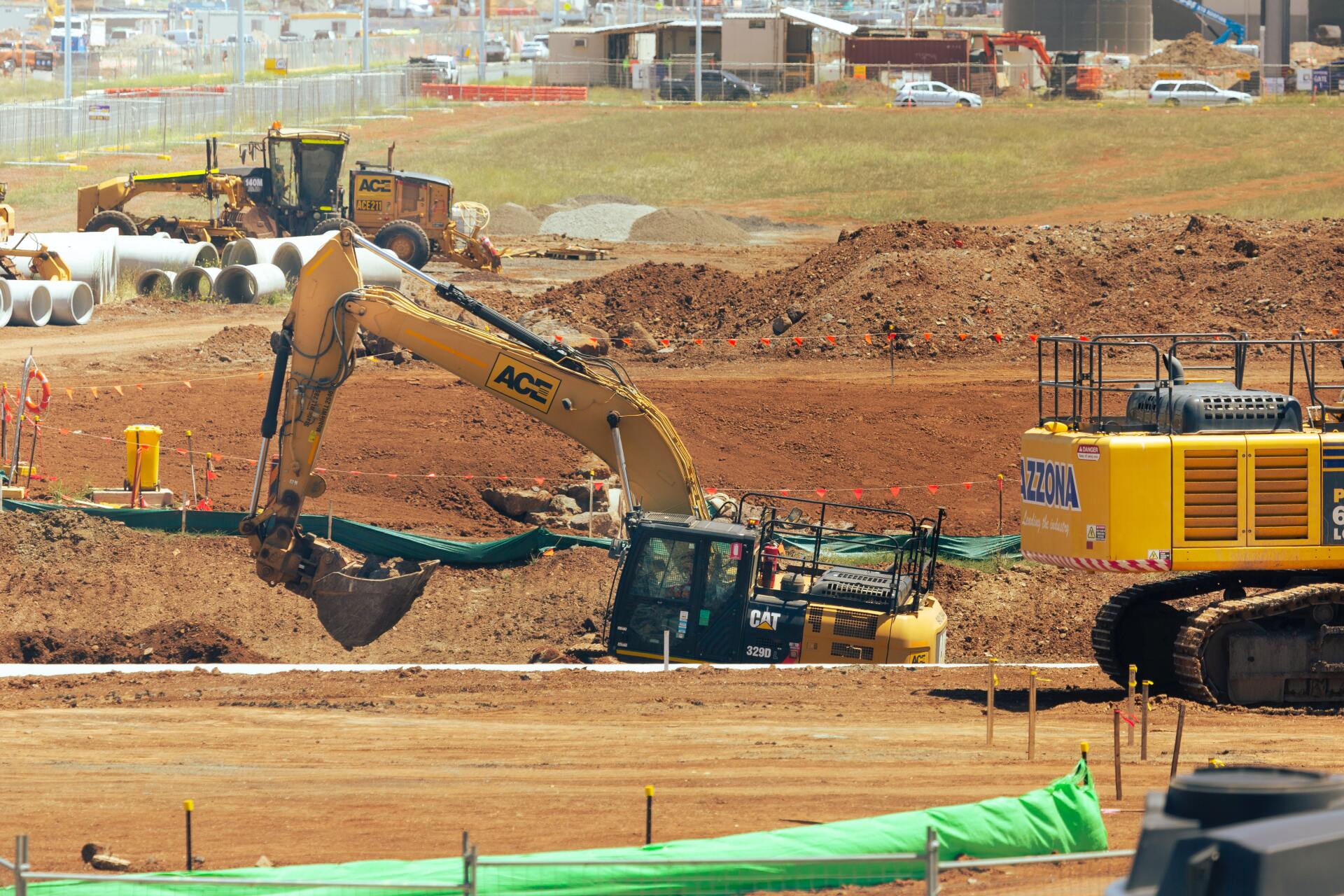 A large yellow excavator is digging in a dirt field