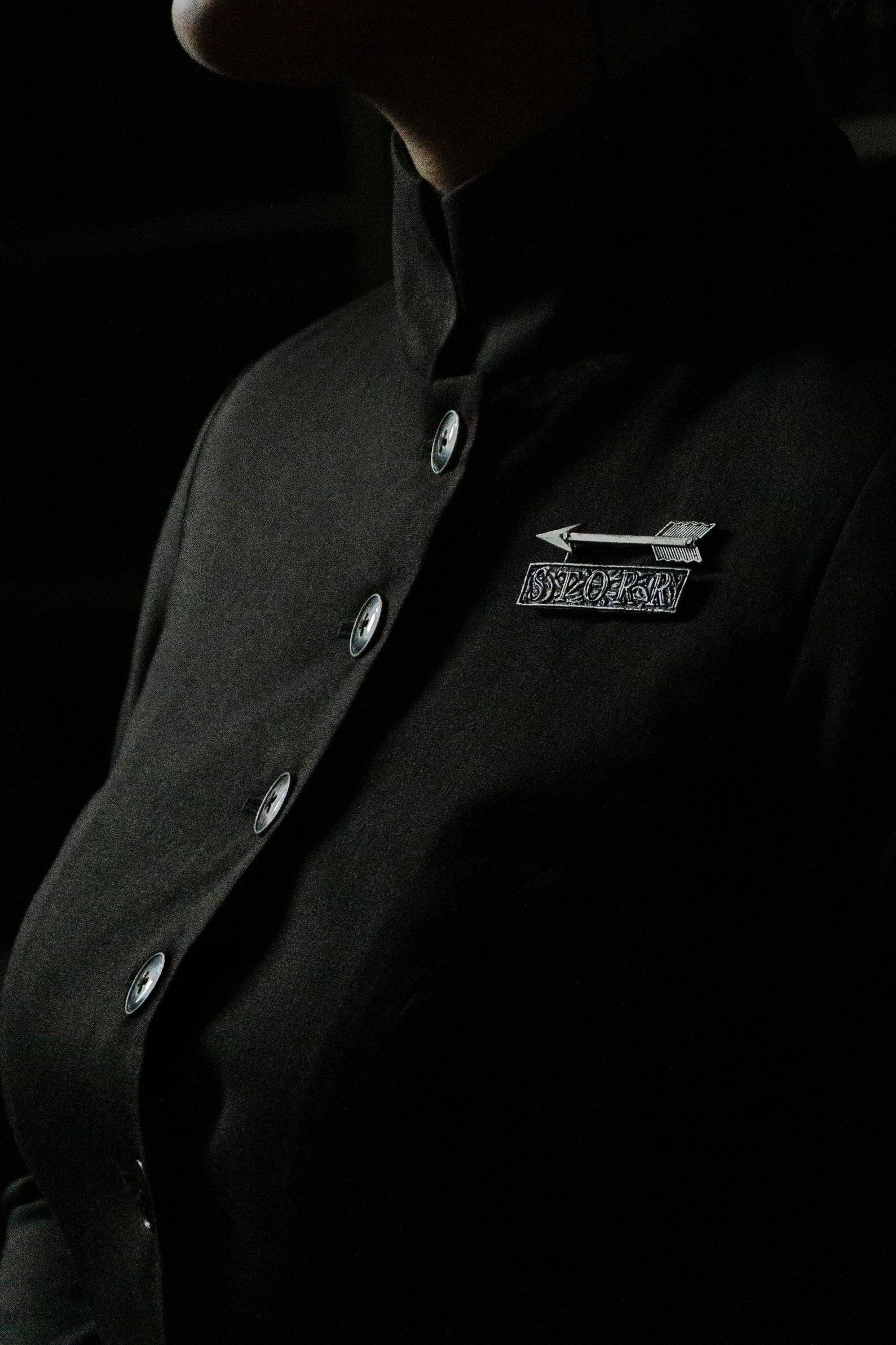 A close up of a woman wearing a dark green suit jacket with a STORR brooch on the left chest.
