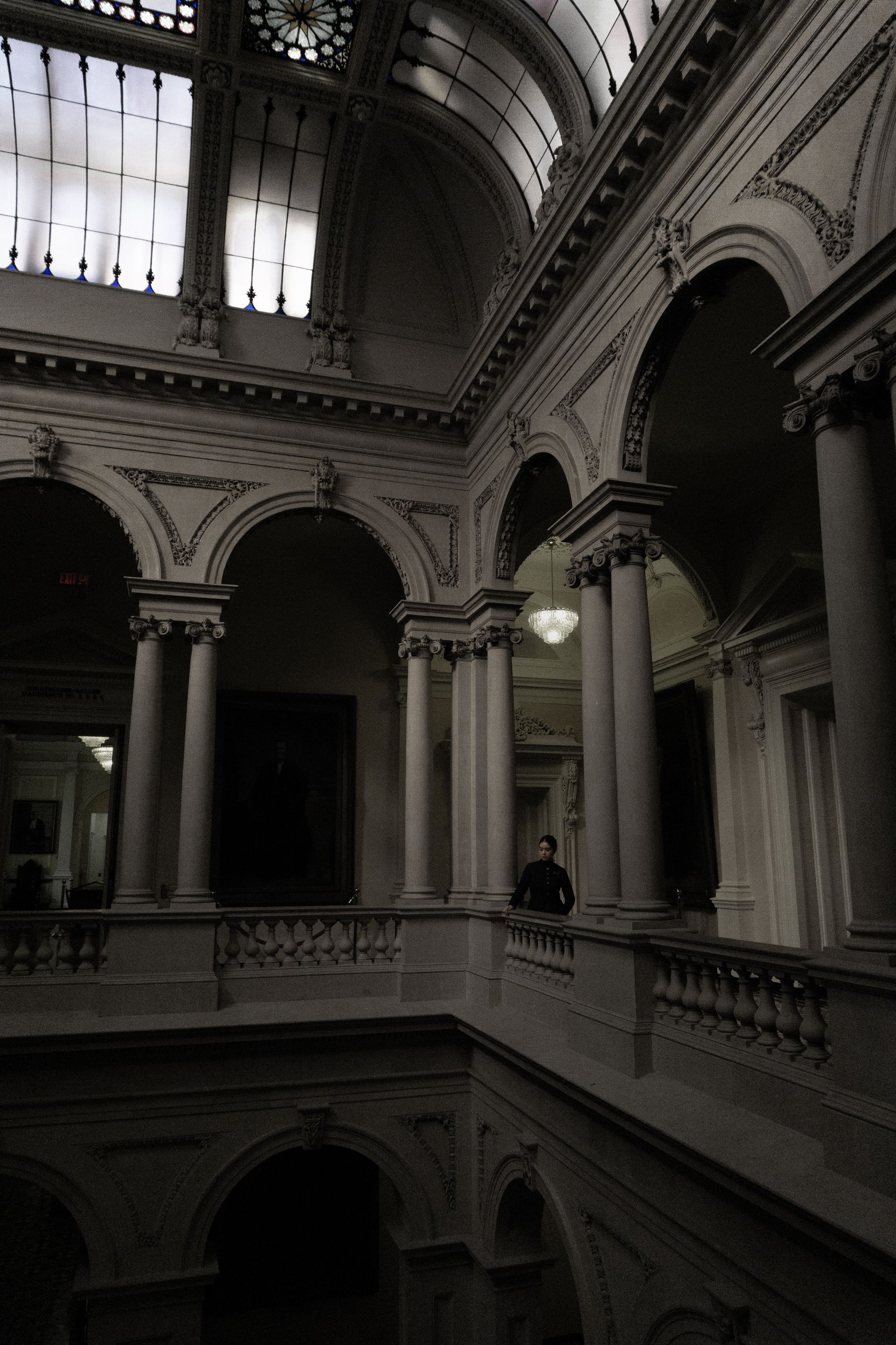 A photo of a woman in a suit standing in the halls of Osgoode Hall, looking over the railing.