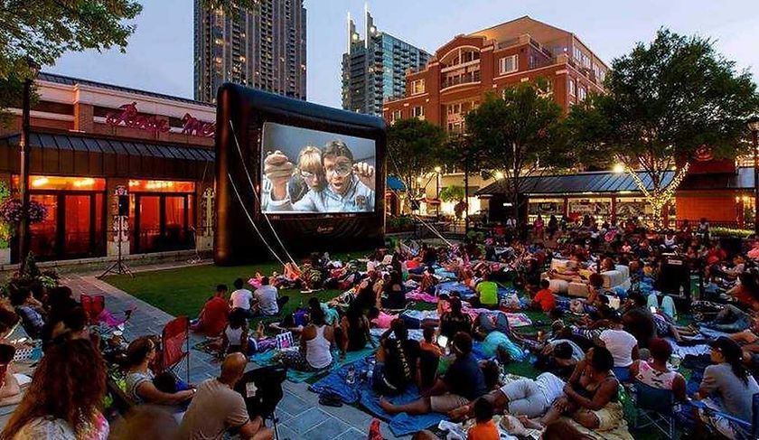 Outdoor movie night with people on blankets watching a film on a large screen in a park.