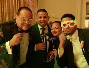 Four people in formal wear pose with novelty glasses and signs at an event.