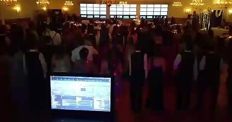 DJ at a dance party. People are dancing in a large room with a lit-up dance floor.