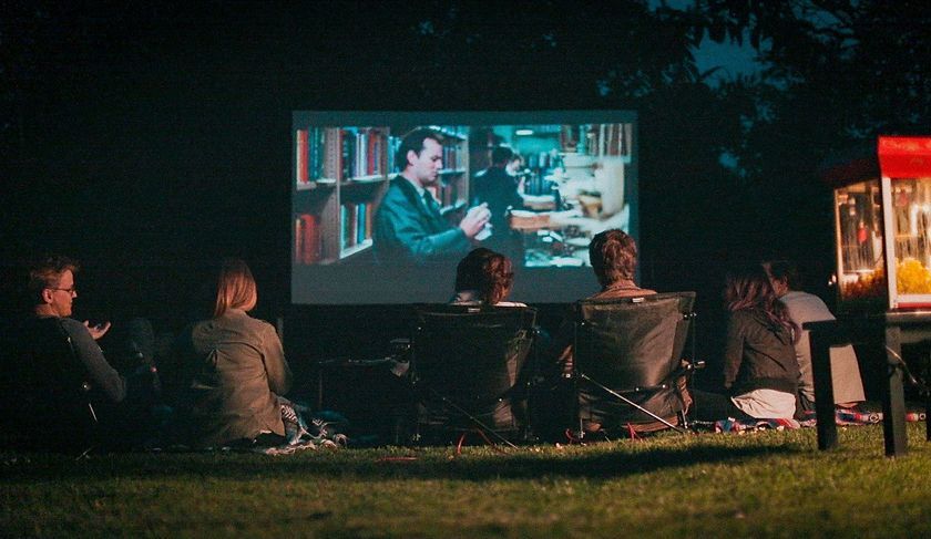 People watching a movie outdoors on a screen in the dark, with a popcorn machine nearby.