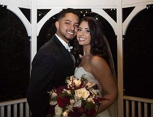 Couple in wedding attire smiling, posing in a gazebo. The bride holds a bouquet.