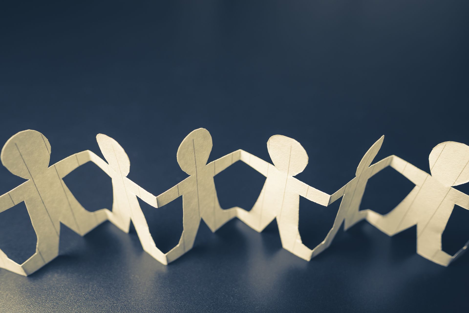 Paper cut-out figures holding hands in a chain against a dark blue background.