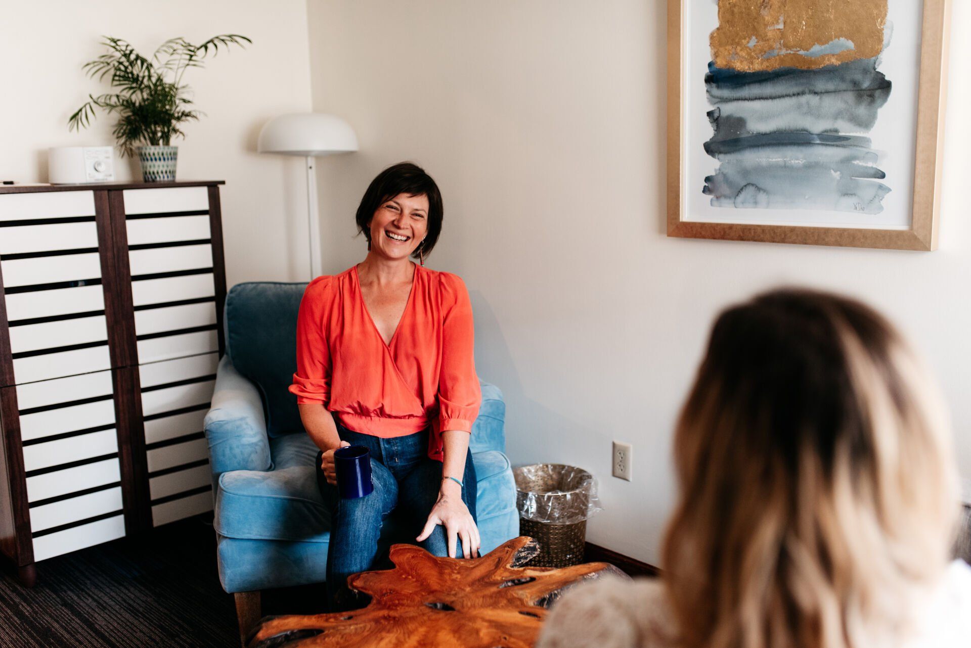 Professional photograph of a woman sitting in a chair and laughing with a cup of coffee. 