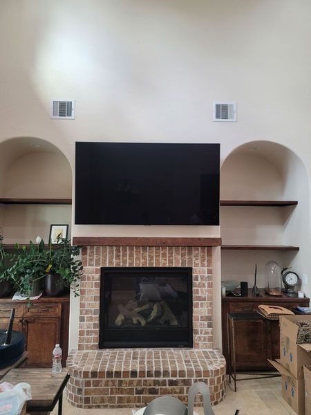 A fireplace with a mounted TV above, flanked by arched shelves. Brick hearth and neutral-colored walls.