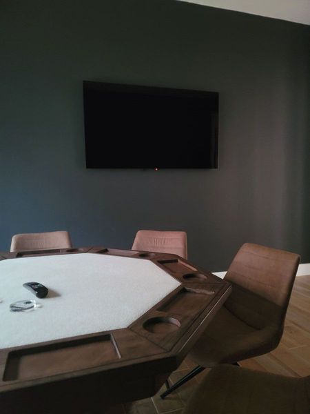Dark wall with a mounted TV over a poker table and chairs.
