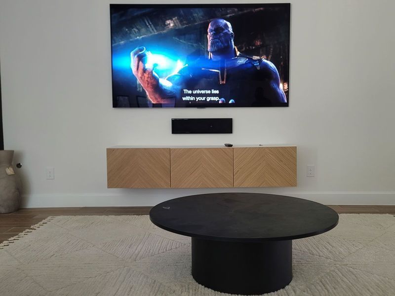 Room with floating TV, soundbar, and console. Thanos on screen, round black coffee table, rug.