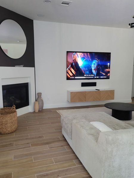 Living room with floating TV and console above a beige couch. Wooden floor and a round coffee table.