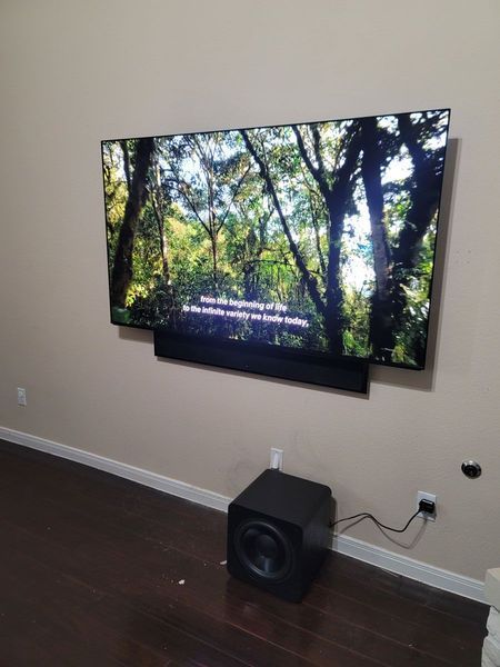 A large TV mounted on a wall with a soundbar below and a subwoofer on the floor.